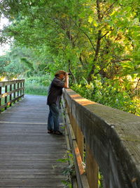 Side view of man standing on footbridge in forest