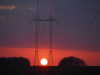 Low angle view of silhouette electricity pylon on field against sky at sunset