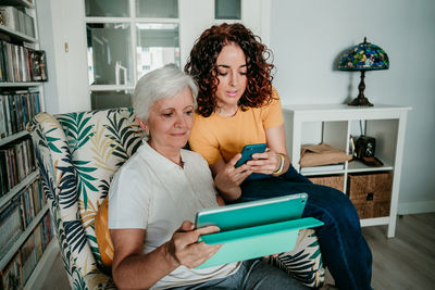 Woman showing smart phone to mother sitting on armchair