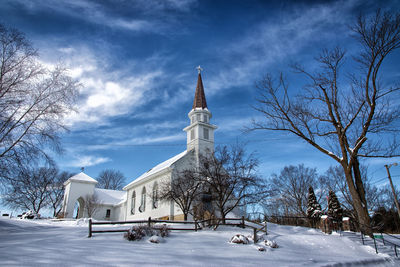 Bare trees in front of church against sky during winter