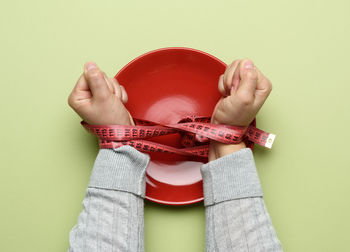 Two female hands tied with green measuring tape on a red round ceramic plate, slimming concep