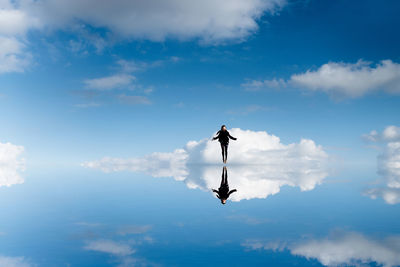 Digital composite image of young woman levitating over calm lake in blue sky