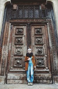 Full length portrait of young woman standing against building