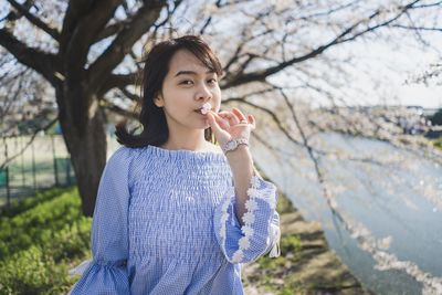 Portrait of woman holding flower while standing against tree