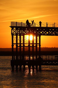 Silhouette people on pier over sea against orange sky