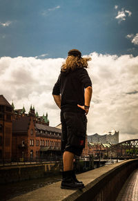 Rear view of man standing on retaining wall by canal