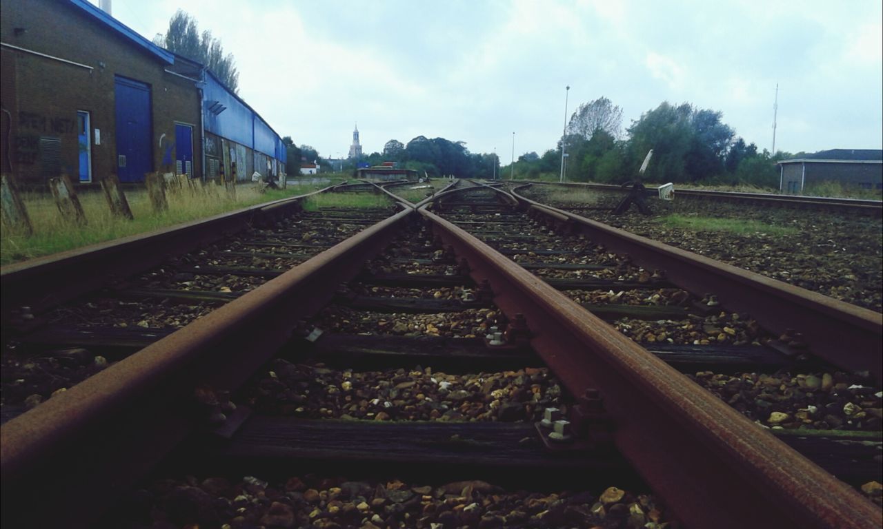 railroad track, rail transportation, transportation, sky, built structure, architecture, building exterior, public transportation, tree, railway track, cloud - sky, day, diminishing perspective, vanishing point, metal, the way forward, outdoors, no people, cloud, field