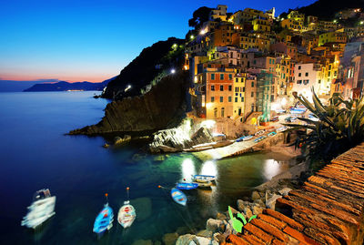 Illuminated buildings by sea against sky in city