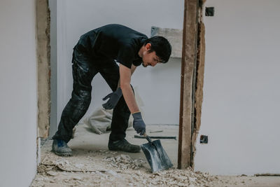 A young man collects construction waste with a dustpan. person