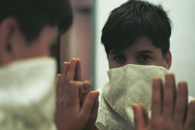 Close-up portrait of young man with obscured face looking in mirror at home