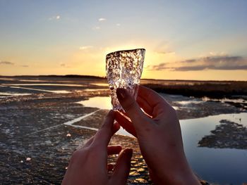 Midsection of person holding ice cream at beach against sky during sunset