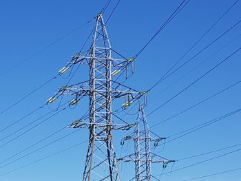 Low angle view of electricity pylon against clear blue sky