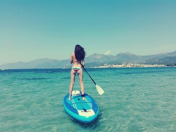 Rear view of woman paddleboarding in sea against blue sky