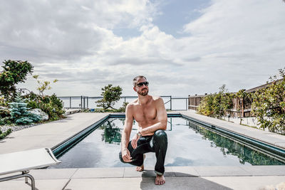 Full length of shirtless young man wearing sunglasses against sky