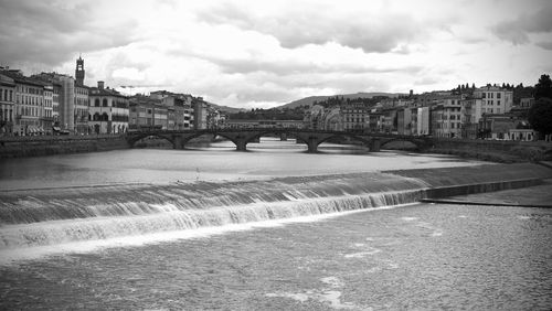 Bridge over river by buildings against sky