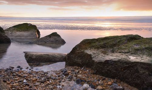 Rocks on beach against sky during sunset