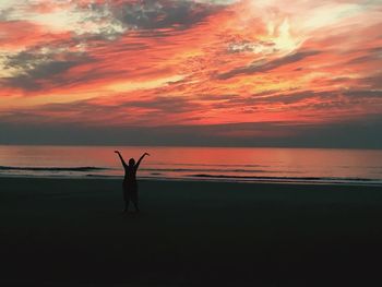 Silhouette person with arms raised standing at beach against sky during sunset