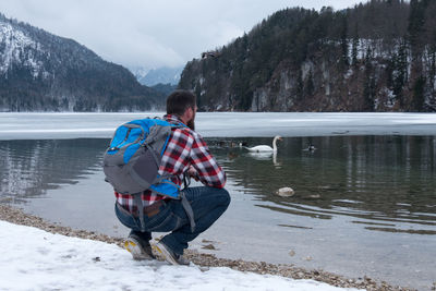 Full length of man crouching by frozen lake during winter