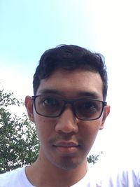 Close-up portrait of young man wearing eyeglasses against sky