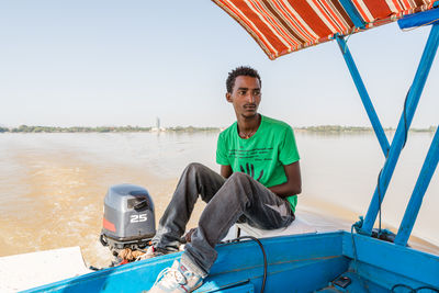 Portrait of smiling man sitting on sea against sky