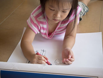 Asian girl painting crayon on large sheets of paper on the floor of her room