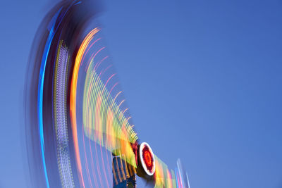 Low angle view of illuminated ferris wheel against clear blue sky