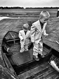Cute boys in full suits standing on moored boat at field