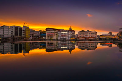 Reflection of buildings in river against sky during sunset