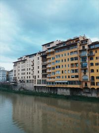 Buildings by river against sky in city