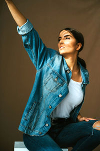 Young woman looking away while sitting against wall