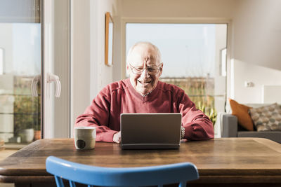 Senior man sitting at home, using laptop
