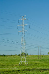 Low angle view of electricity pylon on field against clear sky