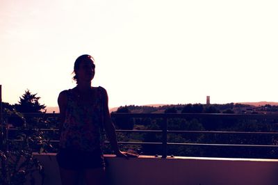 Woman standing by railing against clear sky