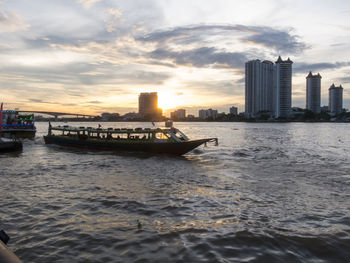 Boat in sea by buildings against sky during sunset