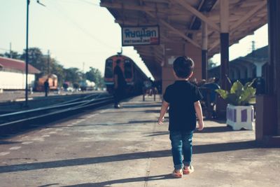 Full length rear view of boy walking at railroad station platform