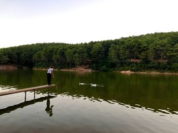 Rear view of man standing by lake against clear sky