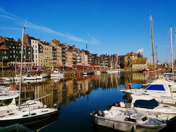 Boats moored by buildings reflecting on sea