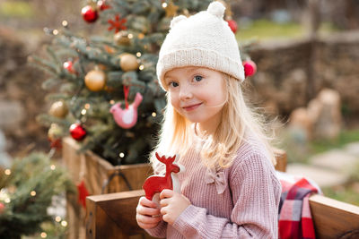 Cute smile kid girl 4-5 year old wear knit hat and sweater decorating christmas tree outdoor closeup