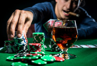 Man playing poker with whiskey and cigar against black background