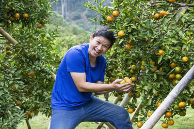 Young man happy harvesting fresh orange fruit garden in hilly area chiangmai, thailand