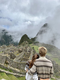 Rear view of couple standing on mountain against sky