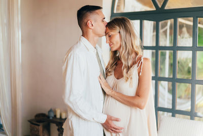 A pregnant couple stands hugging inside.