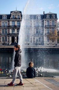 Side view of boy walking against fountain in city