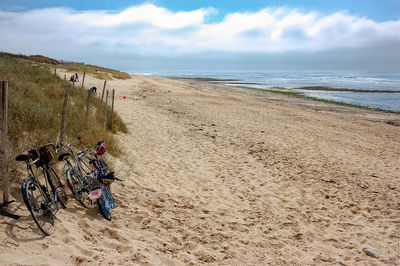 Bicycle parked at beach against cloudy sky