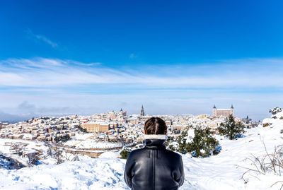 Blonde woman with braids observing the snow-covered city of toledo from a lookout point.