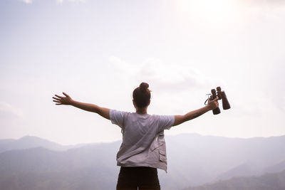 Rear view of man with arms raised against sky during sunset
