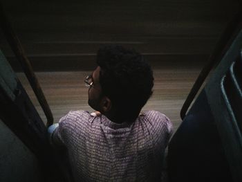 Rear view of man sitting on doorway in train at night