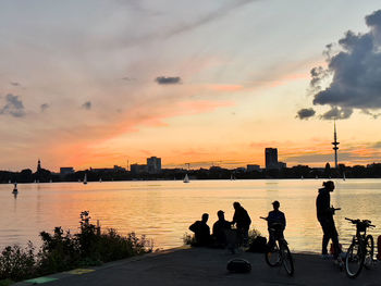 Silhouette people on river against sky during sunset