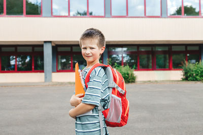  schoolboy boy with a backpack on his back and textbooks in his hands against the school