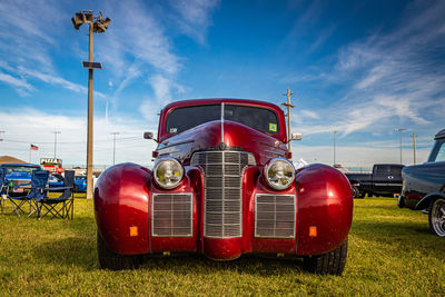 Red vintage car on field against sky